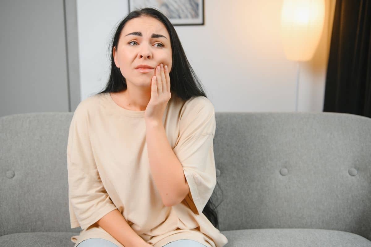 Woman with hand on cheek experiencing gum irritation and discomfort at home.